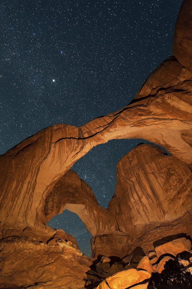 The Milky Way and thousands of stars glow brightly in the night sky above Double Arch in Arches National Park, Utah