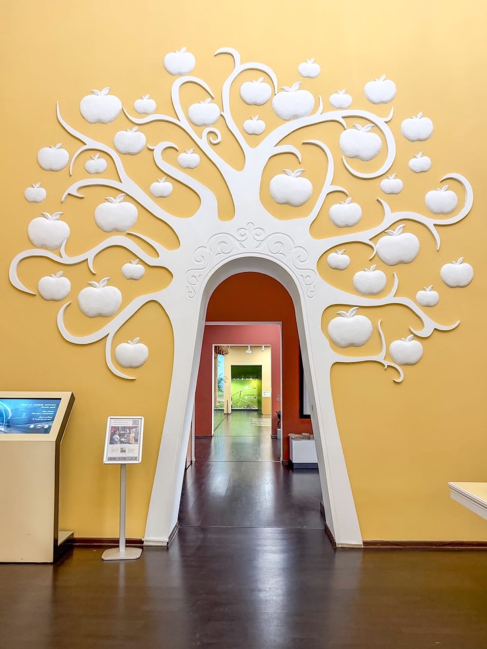 Inside a museum with a yellow wall and an apple tree on the wall