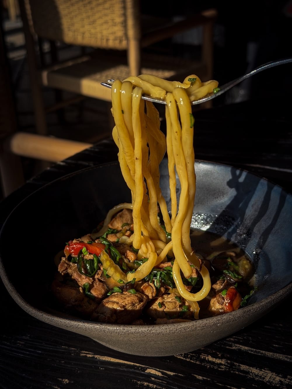 a spoon lifting up handpulled noodles form a bowl