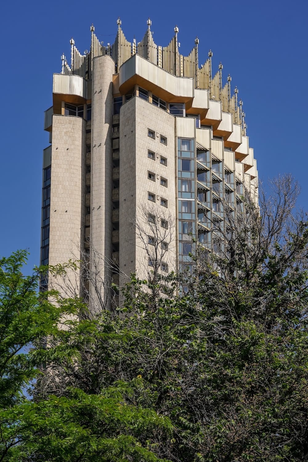 a soviet era tall hotel with a crown on top under a blue sky