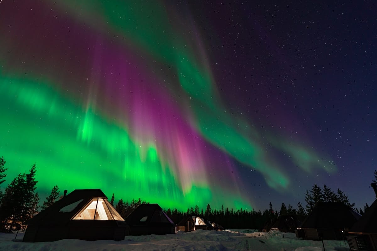 a photo of colorful northern lights over glass igloos in finland