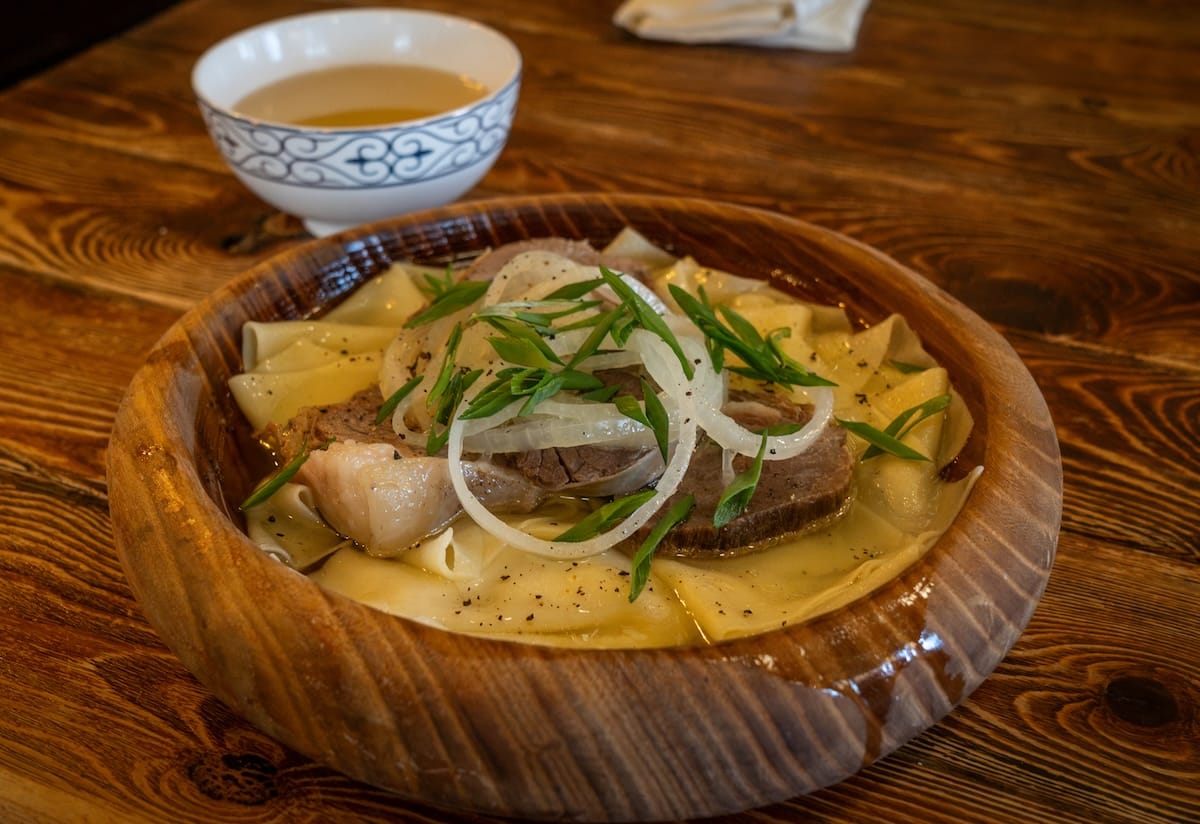 a plate of horsemeat and onions and potatoes with a bowl of broth behind it
best restaurants in almaty, kazakhstan
