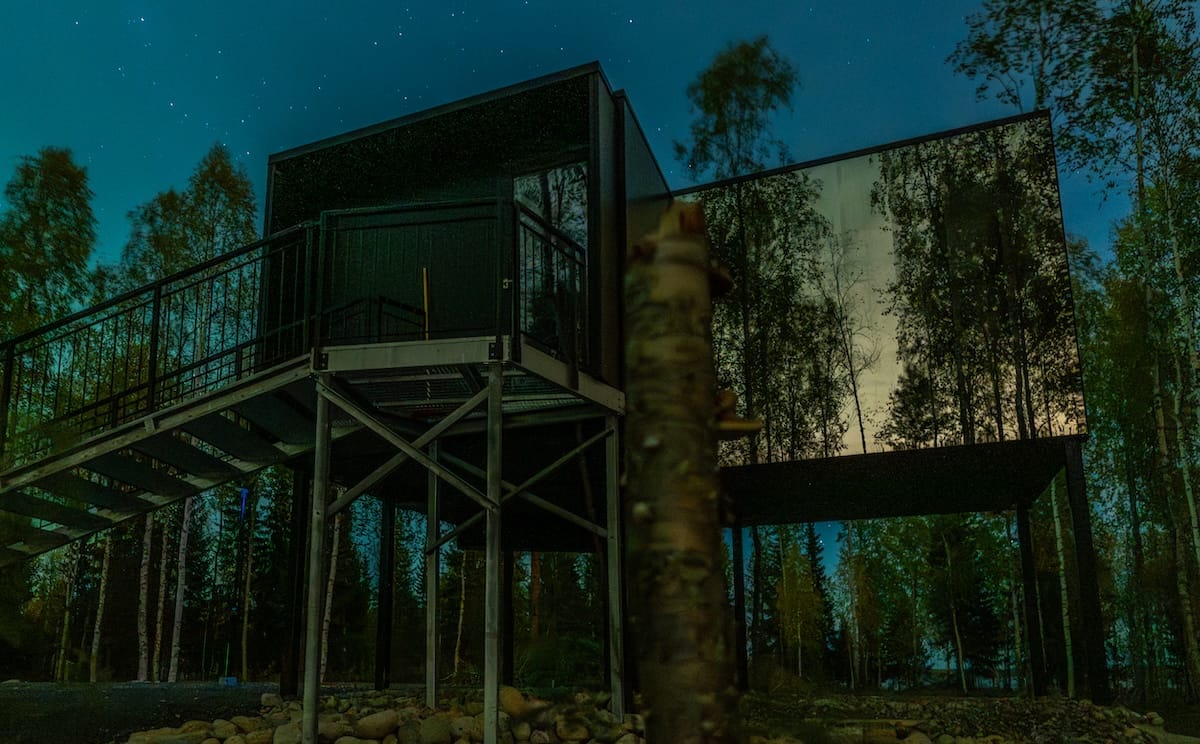 a picture of a glass cabin at a resort with the northern lights in the background