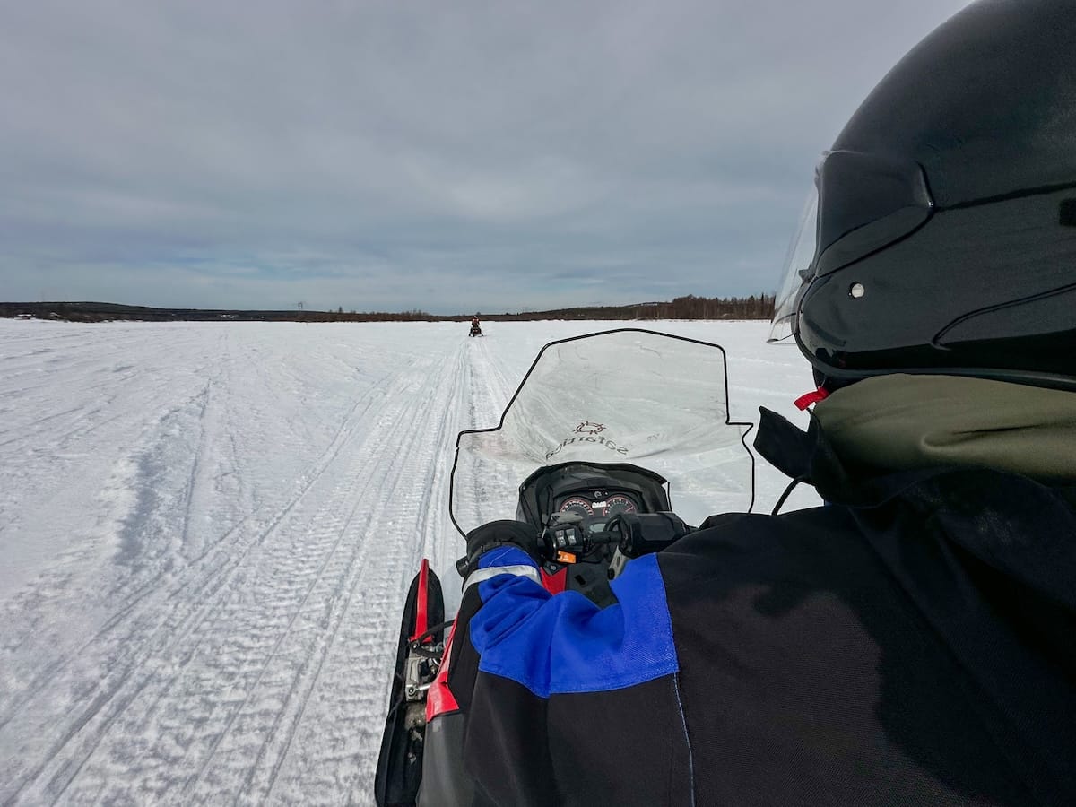 a man snowmobiling on a frozen river in lapland