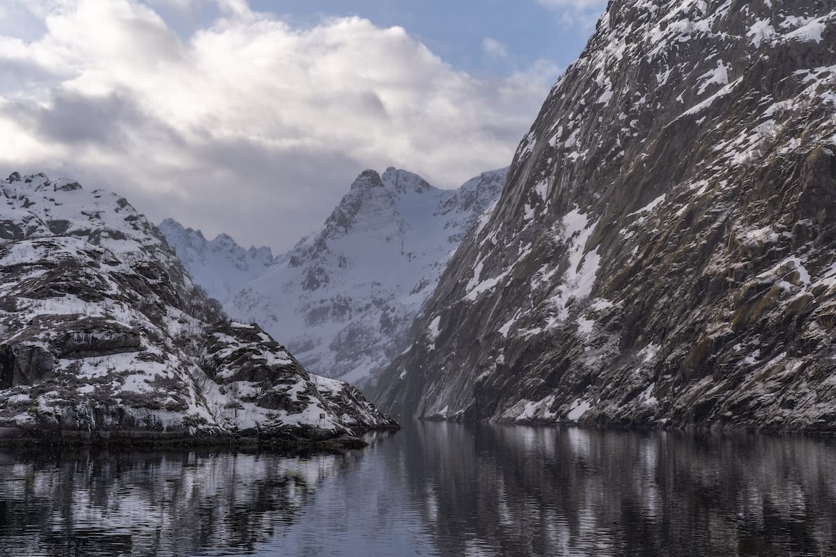 Narrow Trollfjord in the Lofoten Islands in winter, with steep snow-dusted rock walls on both sides, calm reflective water, and a snowy mountain peak ahead