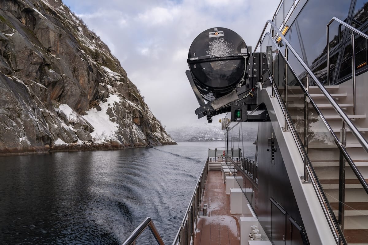 Cruise boat sailing into the narrow Trollfjord in Lofoten in winter, with a steep snow-dusted rock wall on one side and snowy mountains ahead