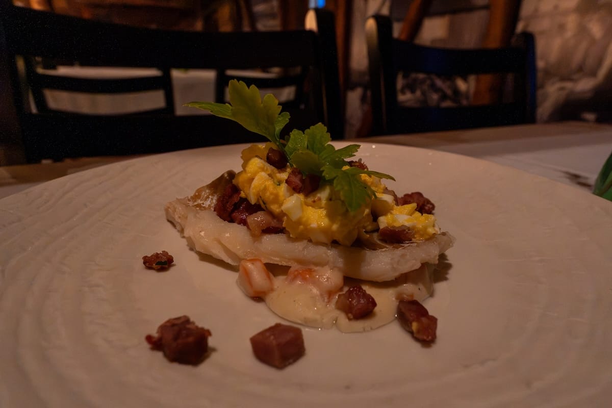 Stockfish dish at Børsen Spiseri in Svolvær, with flaky white fish topped with chopped egg, diced bacon, and fresh parsley on a creamy sauce, served on a white plate