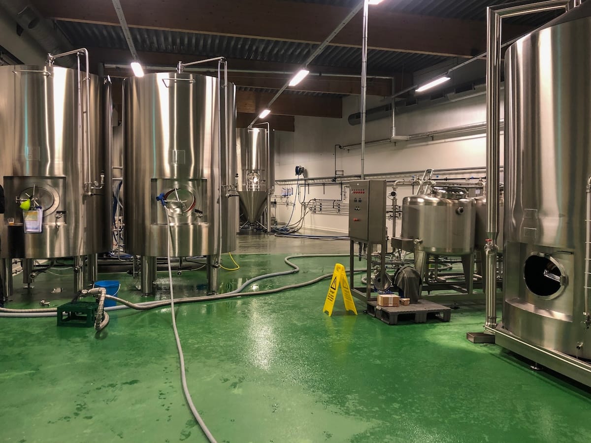 Stainless steel brewing and fermentation tanks on a green floor inside the Lofotpils brewery in Svolvær, Lofoten