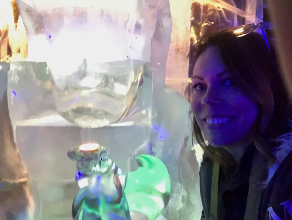 Woman smiling next to a glowing ice sculpture with a small candle at Magic Ice Lofoten in Svolvær