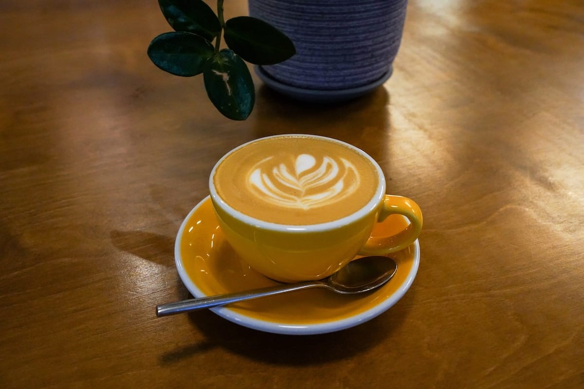a yellow coffee cup with a flat white and latte art on a table