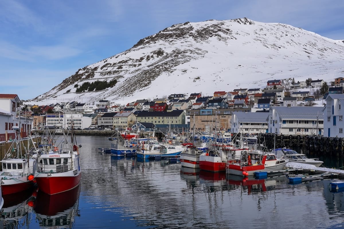 Honningsvåg, Norway's colorful harbor during early April. There are several boats and views of a mountain in the background.