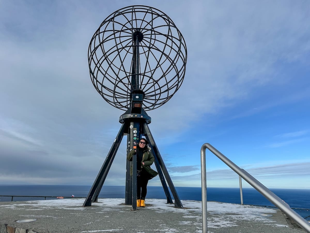 This is a girl (me) posing with the globe in the back of the North Cape Visitor's Center with blue skies and a lot of wind.

Photo: North Cape, Norway