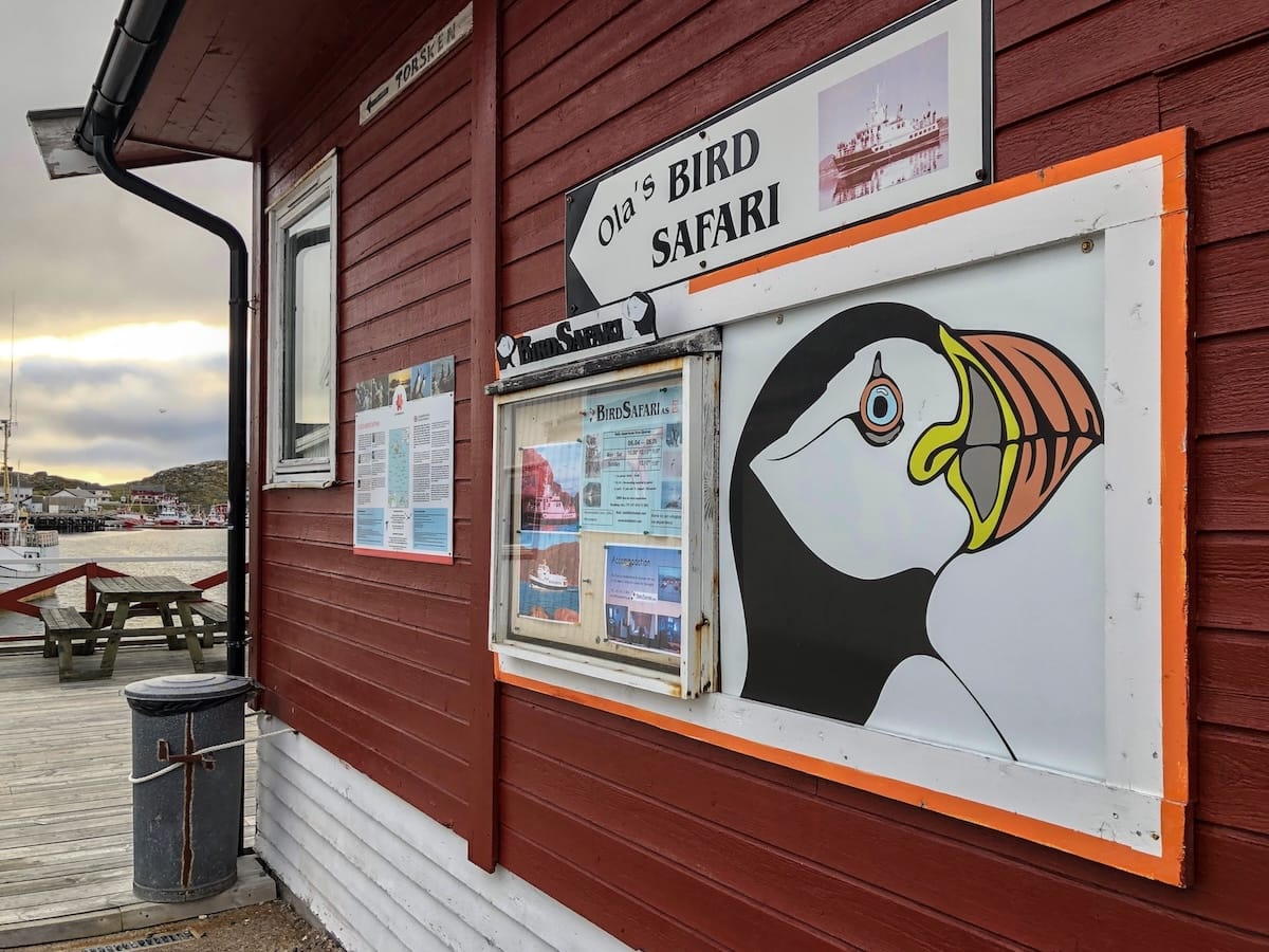 Ola's Bird Safari in Gjesvær - a photo of a picture of a puffin and Ola's branding on a red building with cloudy skies in the background. 

Photo: Gjesvær, Norway