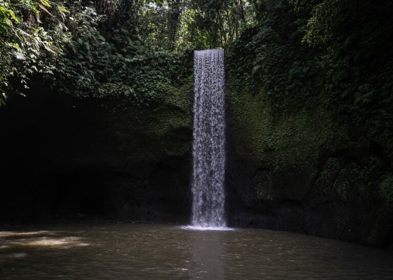 How to Visit Tibumana Waterfall in Bali This is a photo of the waterfall streaming down into a brown pool of water.