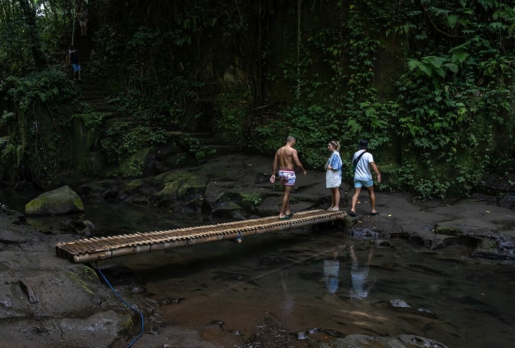 A bamboo crossing with two people hanging out on the bridge in Bali at Kanto Lampo Waterfall