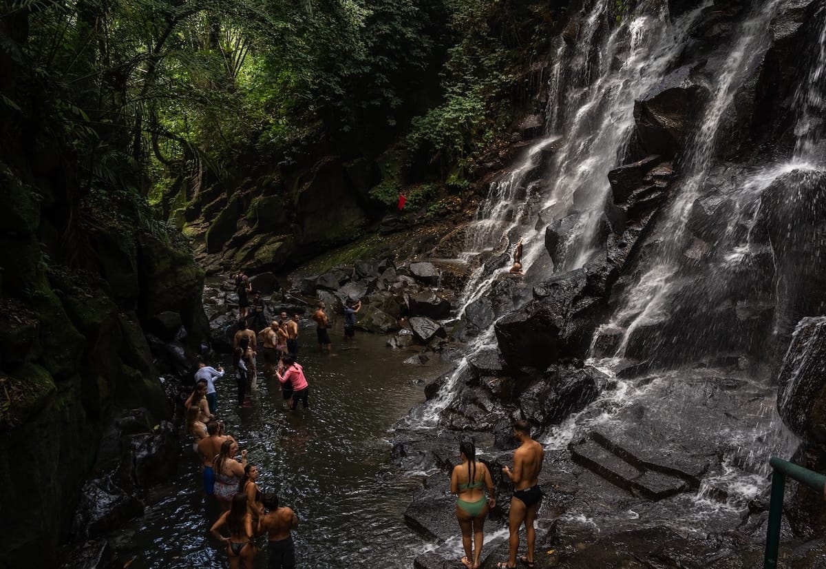 The line of people standing in water waiting for a photo at Kanto Lampo Waterfall in Bali