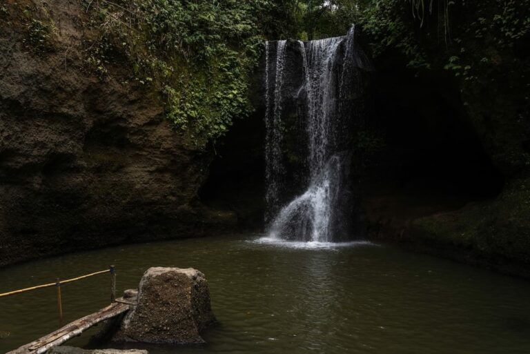 Everything to know before visiting Suwat Waterfall in Bali This is a photo of a waterfall that is not flowin that powerfully in Bali. There is a pool in front of it.