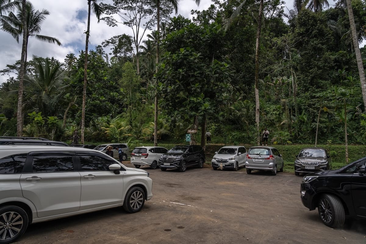 This is a dirt parking lot at Ulu Petanu waterfall with cars in it.