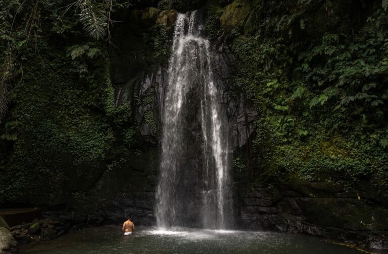 How to visit Ulu Petanu Waterfall in Bali This is a waterfall flowing into a pool with a man standing beside it