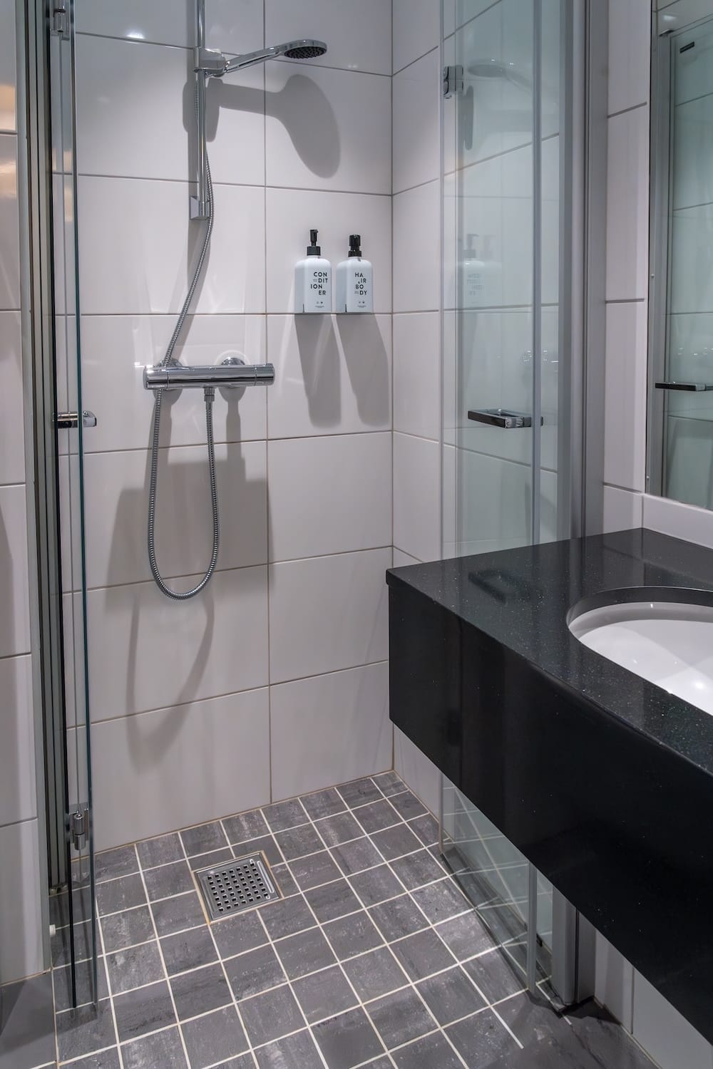 Shower in the room at Scandic Bryggen.
This is a photo of a shower in a white-tiled bathroom with a black sink.