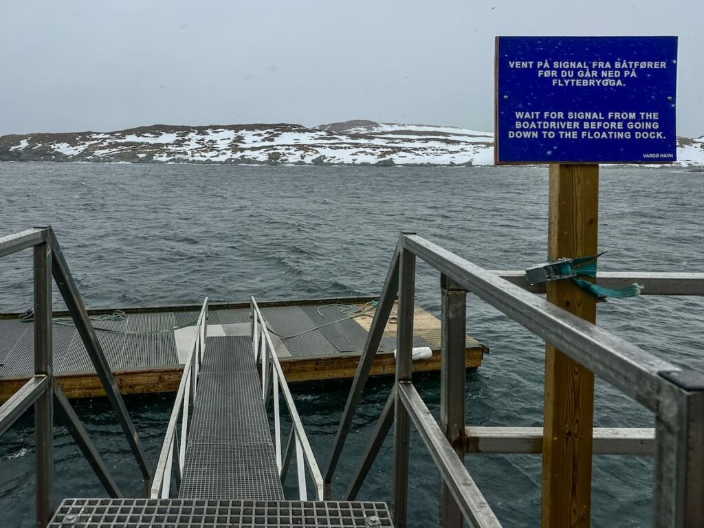 A dock in Hornøya Norway where you will arrive by boat. There is a blue sign in front of it with Norwegian on it.