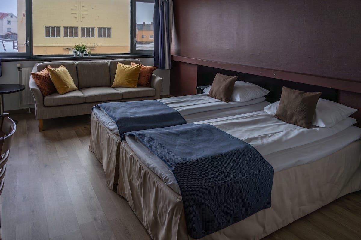 A photo of an outdated hotel room in Norway. There are two beds and a couch.