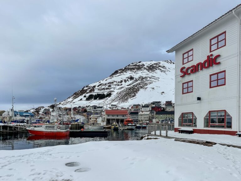 Scandic Bryggen Review - a stay on the harbor in Honningsvåg This photo is a picture of the hotel alongside the harbor with snow on the ground and boats in the water.