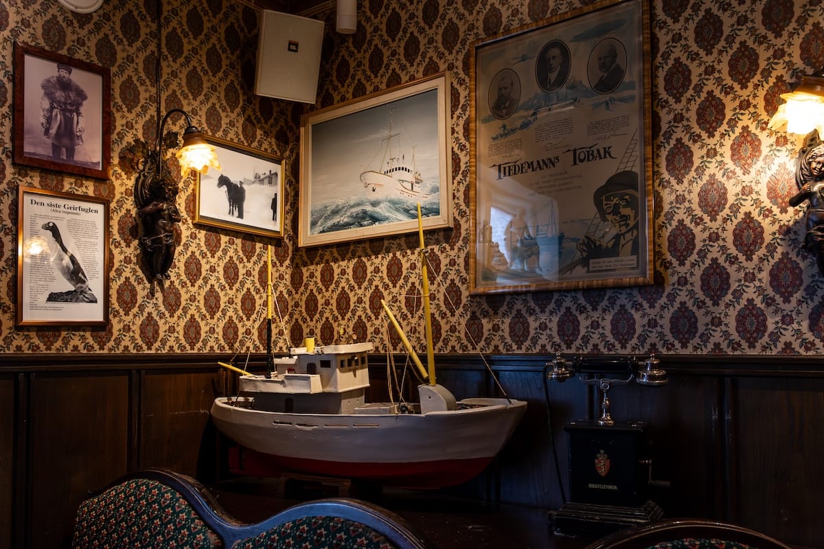 Inside Nordpol Kro pub in Vardø - this pub is dark and cozy and is partly a museum. There is a ship model and historic photos on a wallpapered wall.