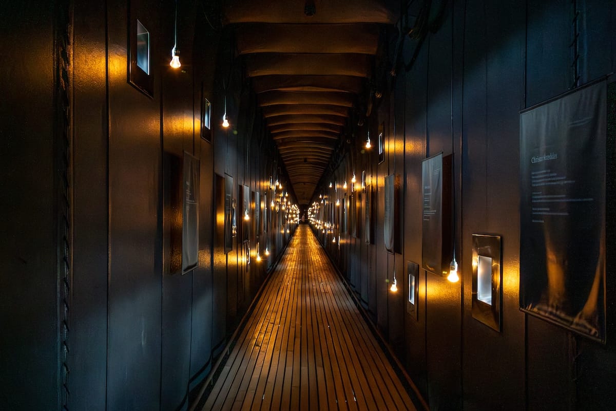 A dark hall with black walls and candles and lights that has information on the walls about those persecuted in the Vardø witch trials