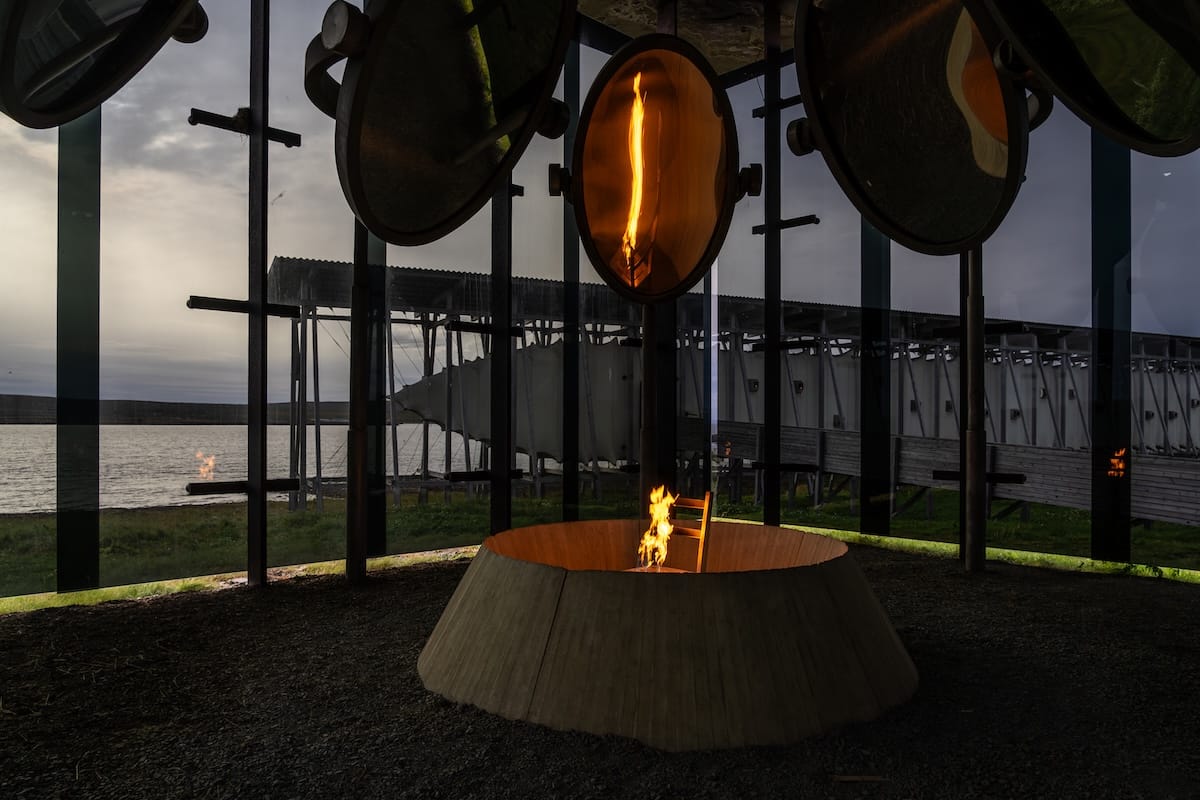 A burning chair in a glass room where you can see the outside and the fjord. The chair symbolizes those burned in the Vardø witch trials.