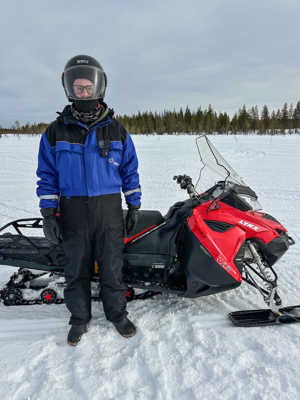 Snowmobiling in Rovaniemi, Finland: Best tours, tips, and what to expect.
Photo: a man standing in front of a snowmobile in Rovaniemi, Finland. He is in a winter suit in a Finnish forest