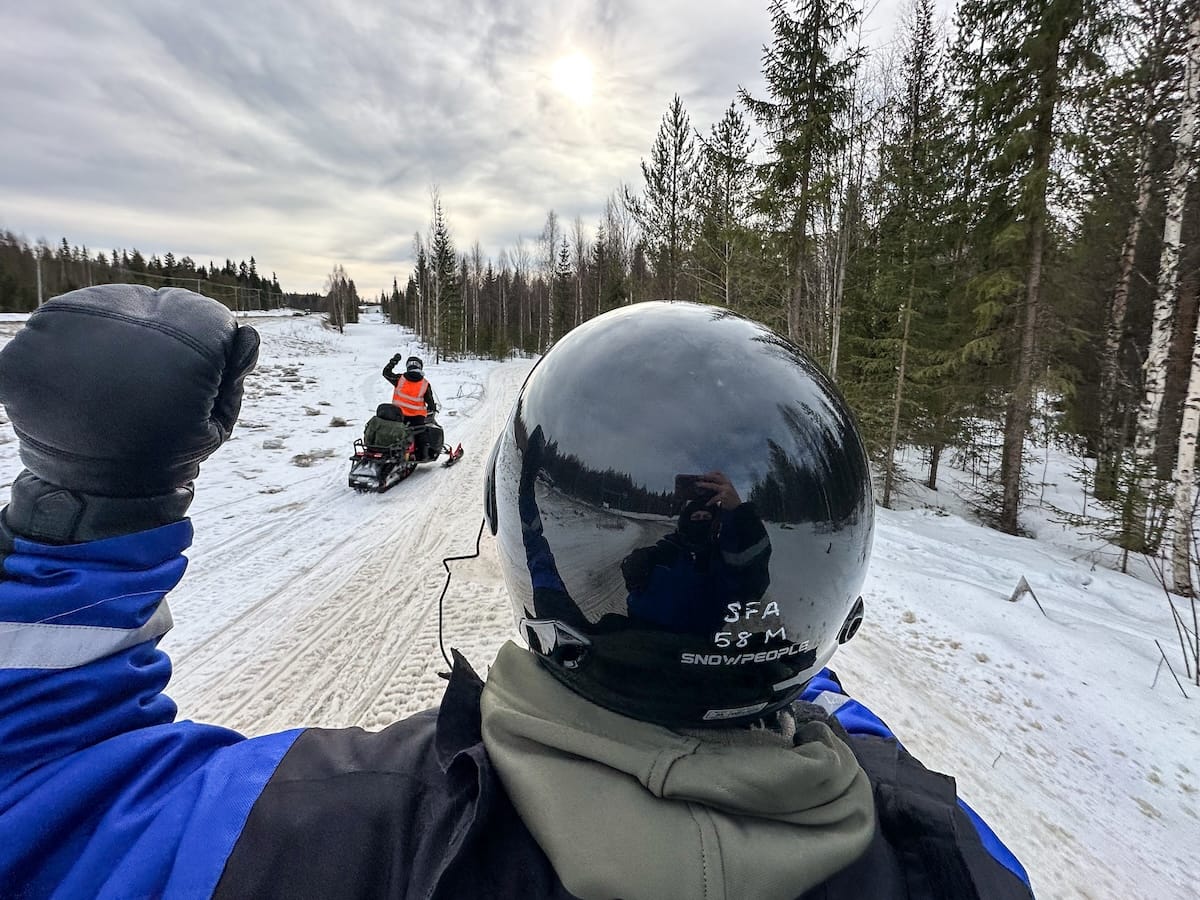 Snowmobiling in Rovaniemi, Finland: Best tours, tips, and what to expect.
Photo: this is a man driving a snowmobile doing the hand signal for stopping and slowing down. The photo is inside a Finnish forest outside of Rovaniemi, Finland.