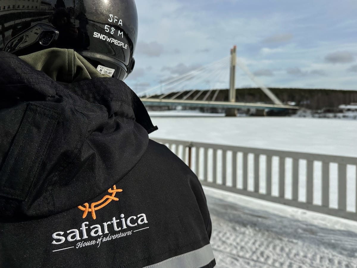Man snowmobiling with Safartica in Rovaniemi, Finland about to head out on the river. There is a bridge in the background.