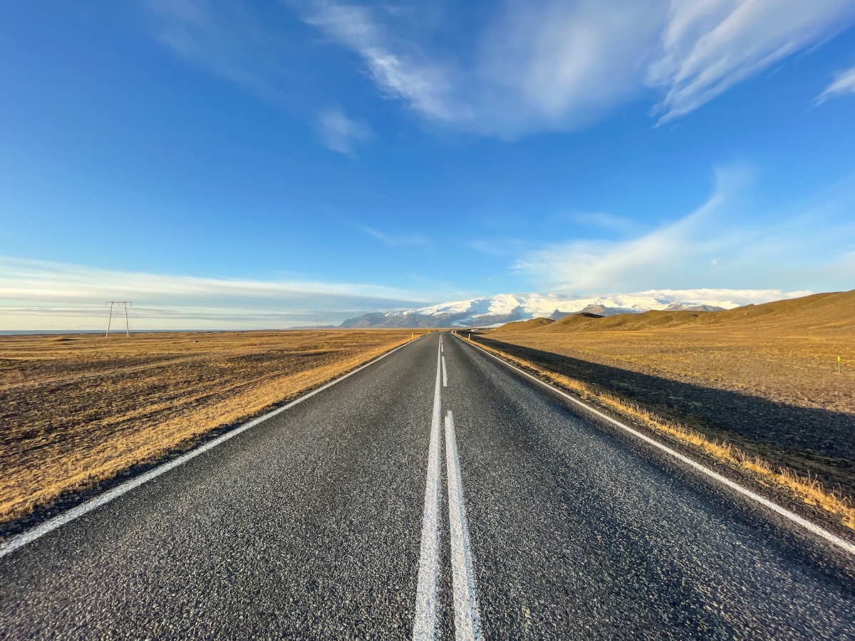 This is a road under a blue sky in Iceland - the scenery is a bit bleak with color but looks vibrant under the sky