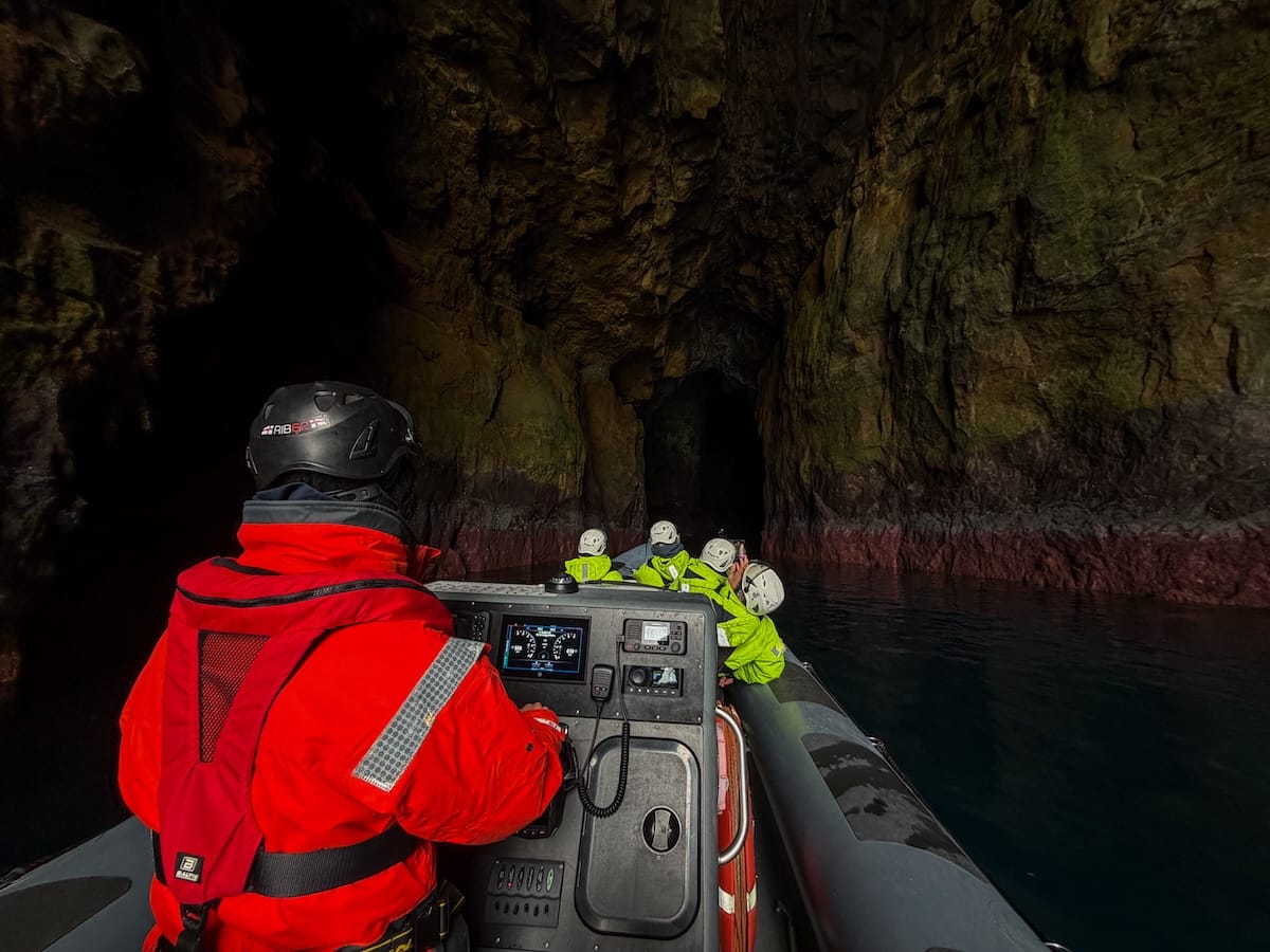 Inside the sea caves of Hestur (a man in an orange suit guiding a RIB boat through sea caves)