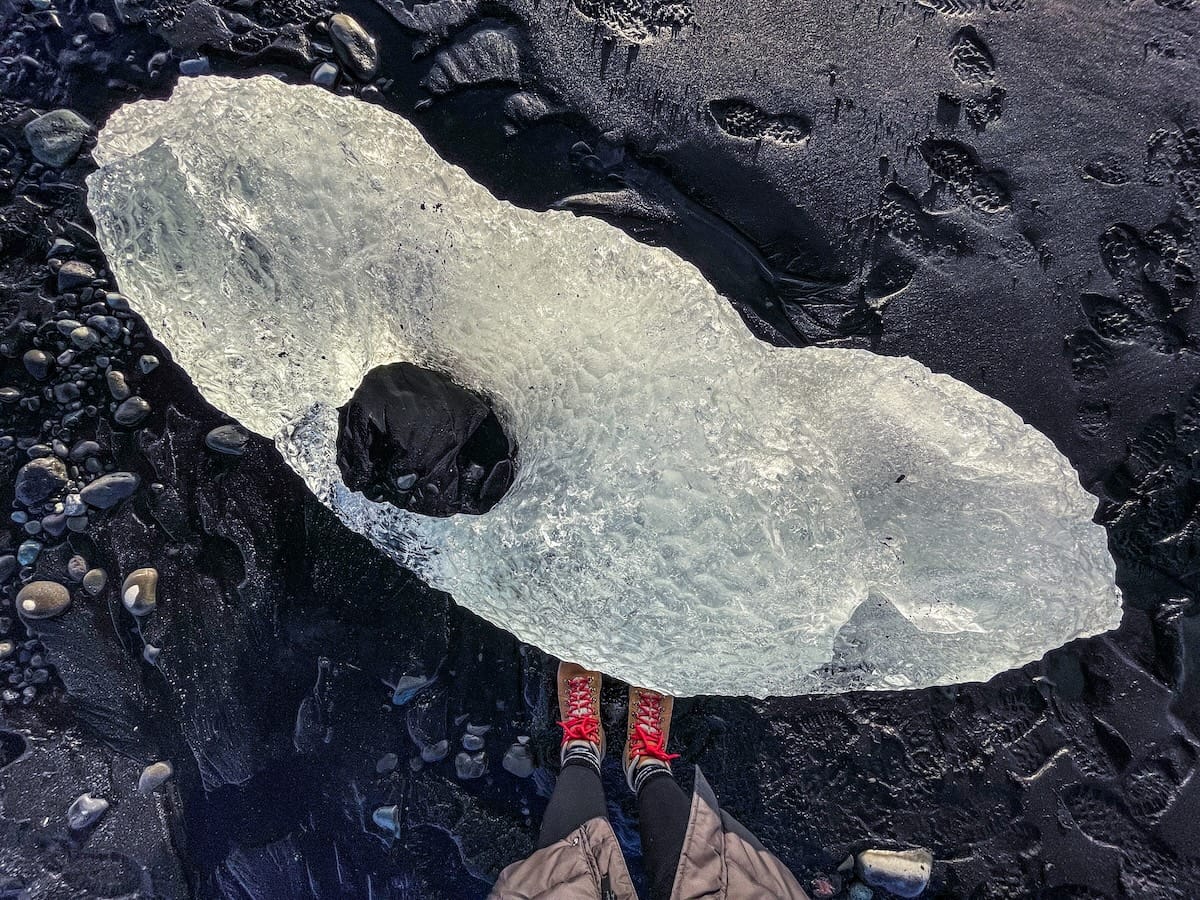 Photo is of an iceberg chunk on a black sand beach in Iceland with a girl's pair of hiking boots with red shoelaces