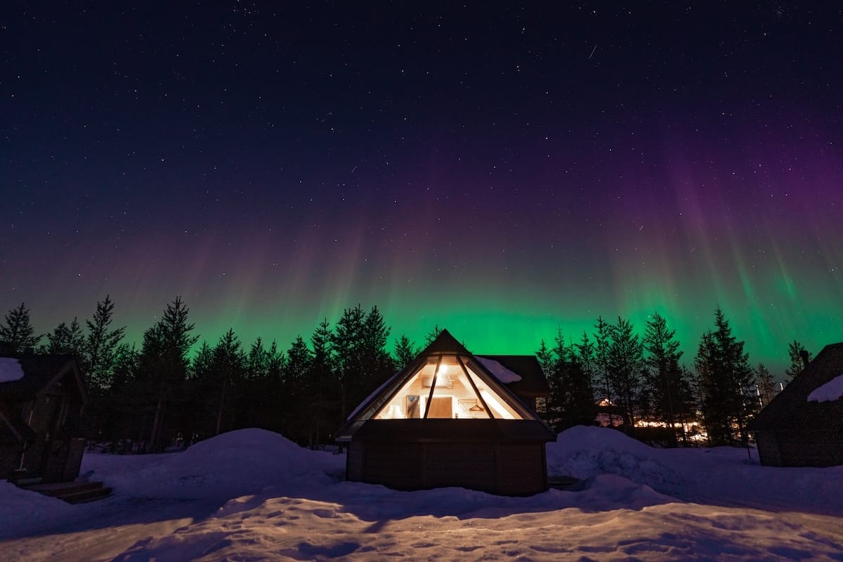 a glass igloo lit up under the northern lights