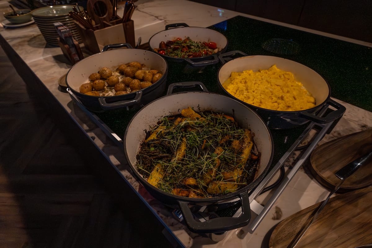 4 dishes with potatoes, sausage and tomatoes, scrambled eggs, and parsnips and broccolini with microgreens covering it on a table