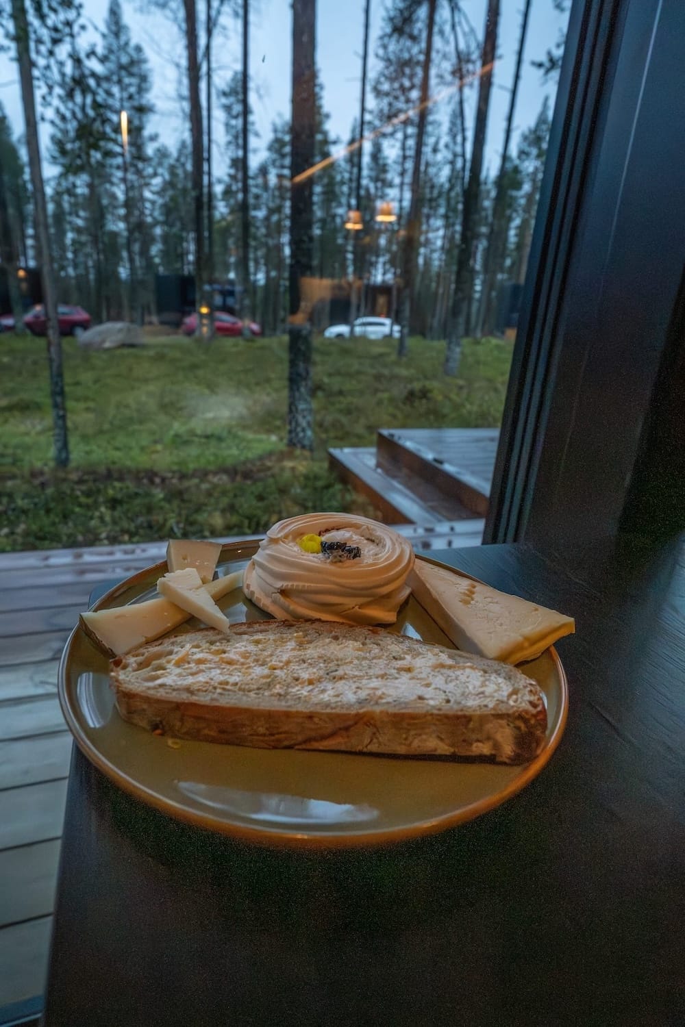 A plate by a window with a pavlova, bread with butter, and a few slices of cheese