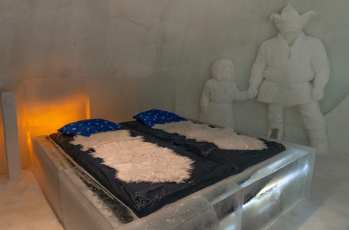 a sami father and son inside a room made from ice with a bed in a ice hotel