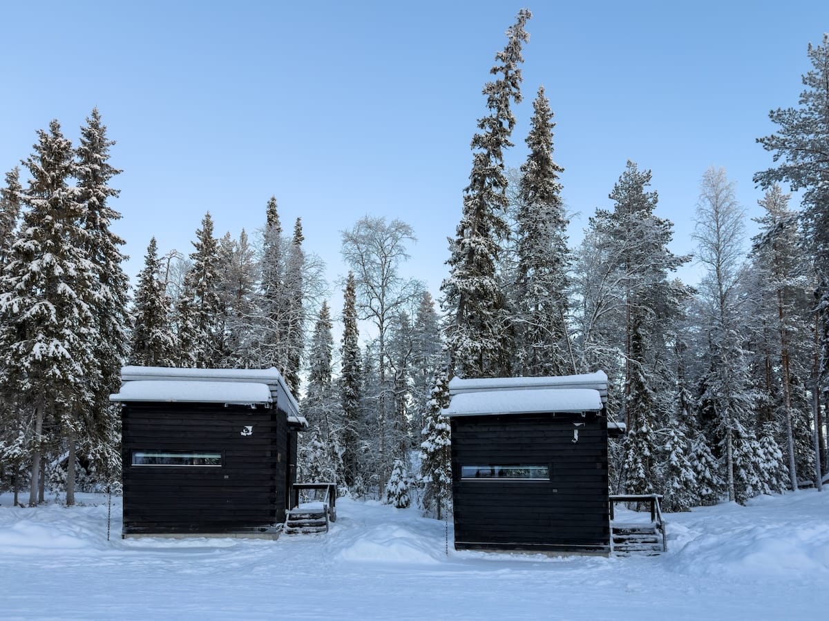 two black square huts in the middle of a snowy finnish forest
