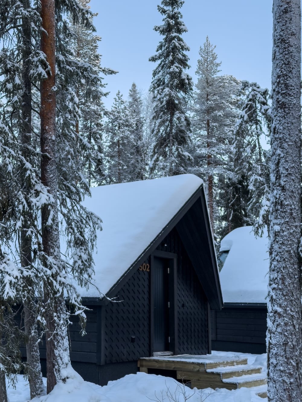 a black painted cabin in the middle of a snowy finnish forest