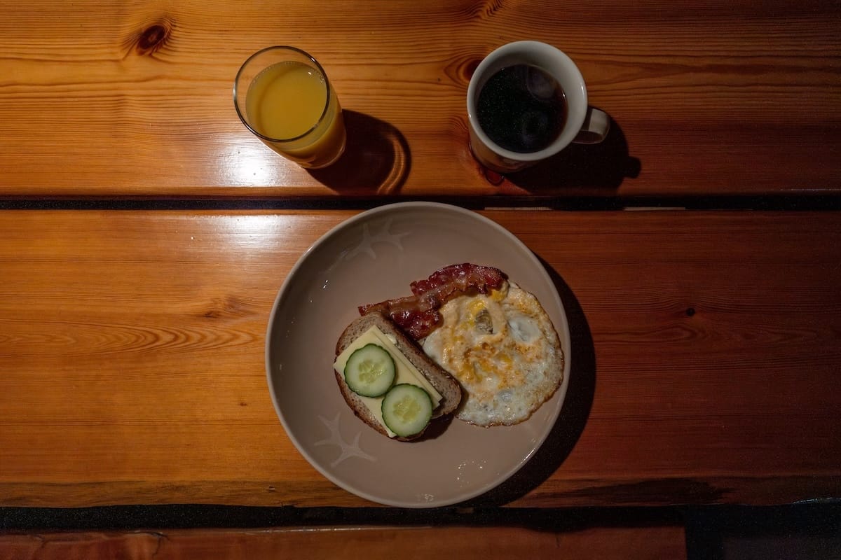 Livo Arctic Resort
_____
A plate with a sandwich topped with cucumbers, an egg, and bacon with an orange juice and coffee in a mug at the top of the photo.