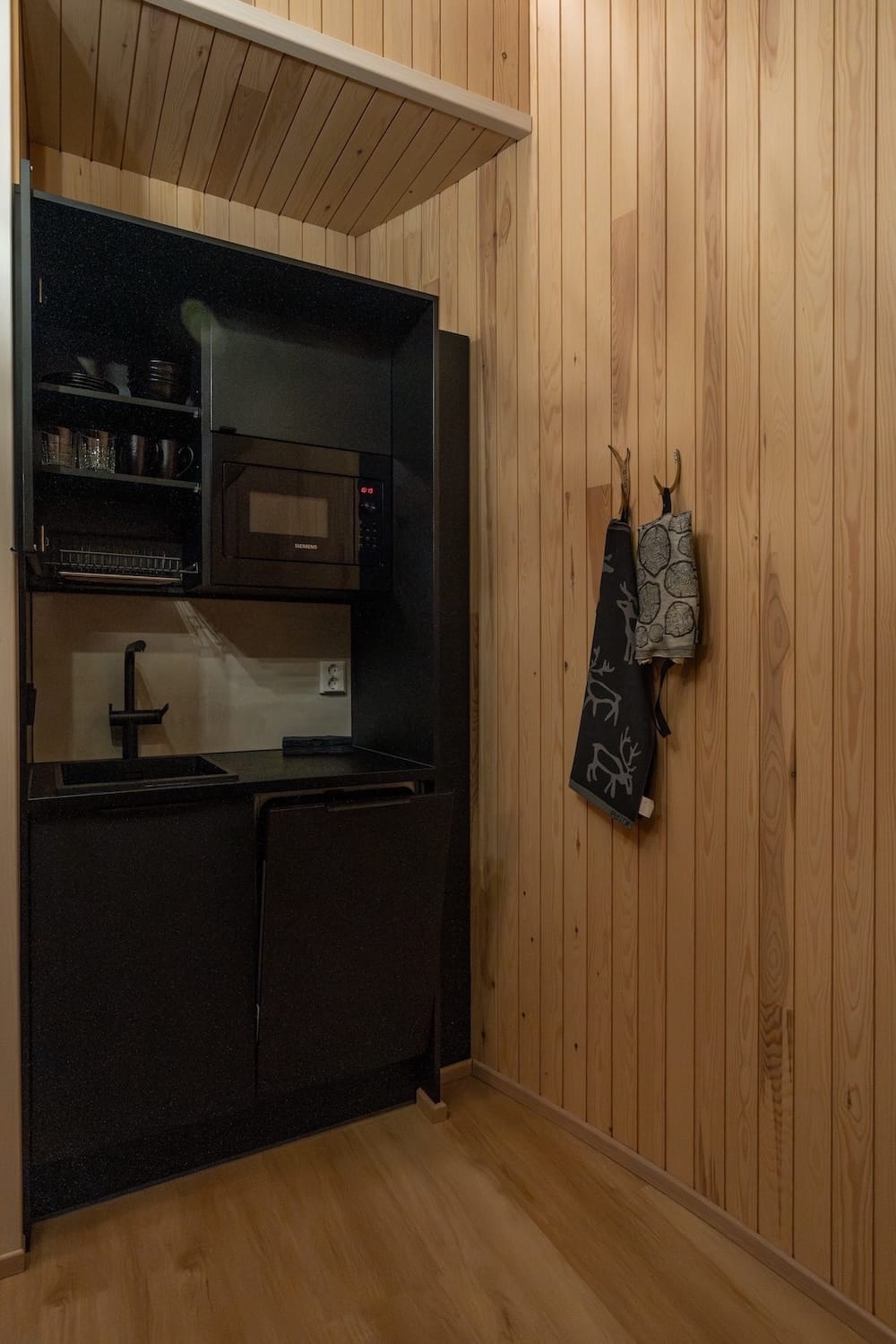 Livo Arctic Resort
_____
A kitchenette area with hanging towels, a microwave, and dark cabinets