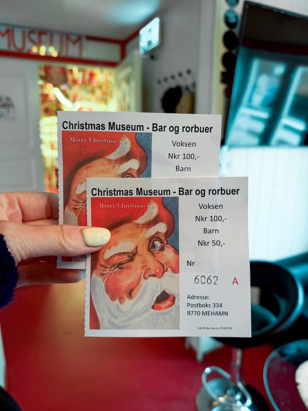 a woman's hand holding two paper tickets to a christmas museum