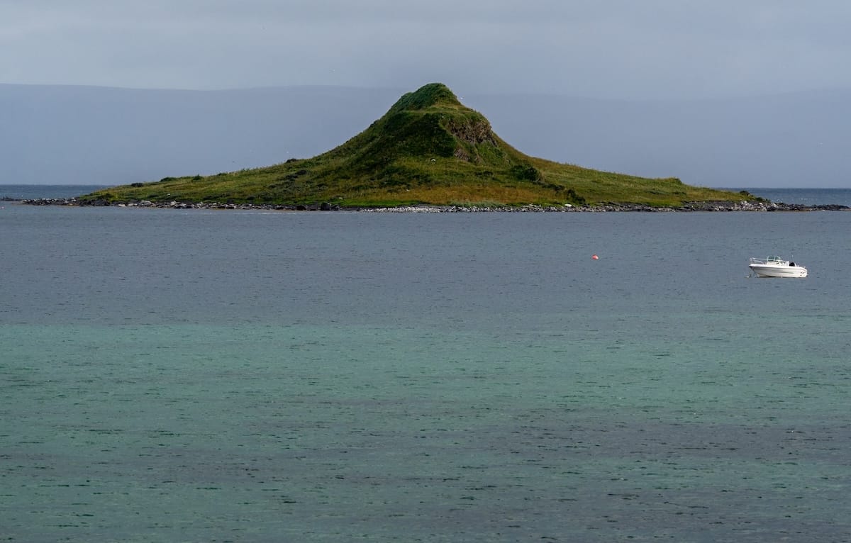 Where to Stay at the North Cape in Norway (+ Honningsvåg)
a cone shaped islet with a ton of birds and a green sea in front of it