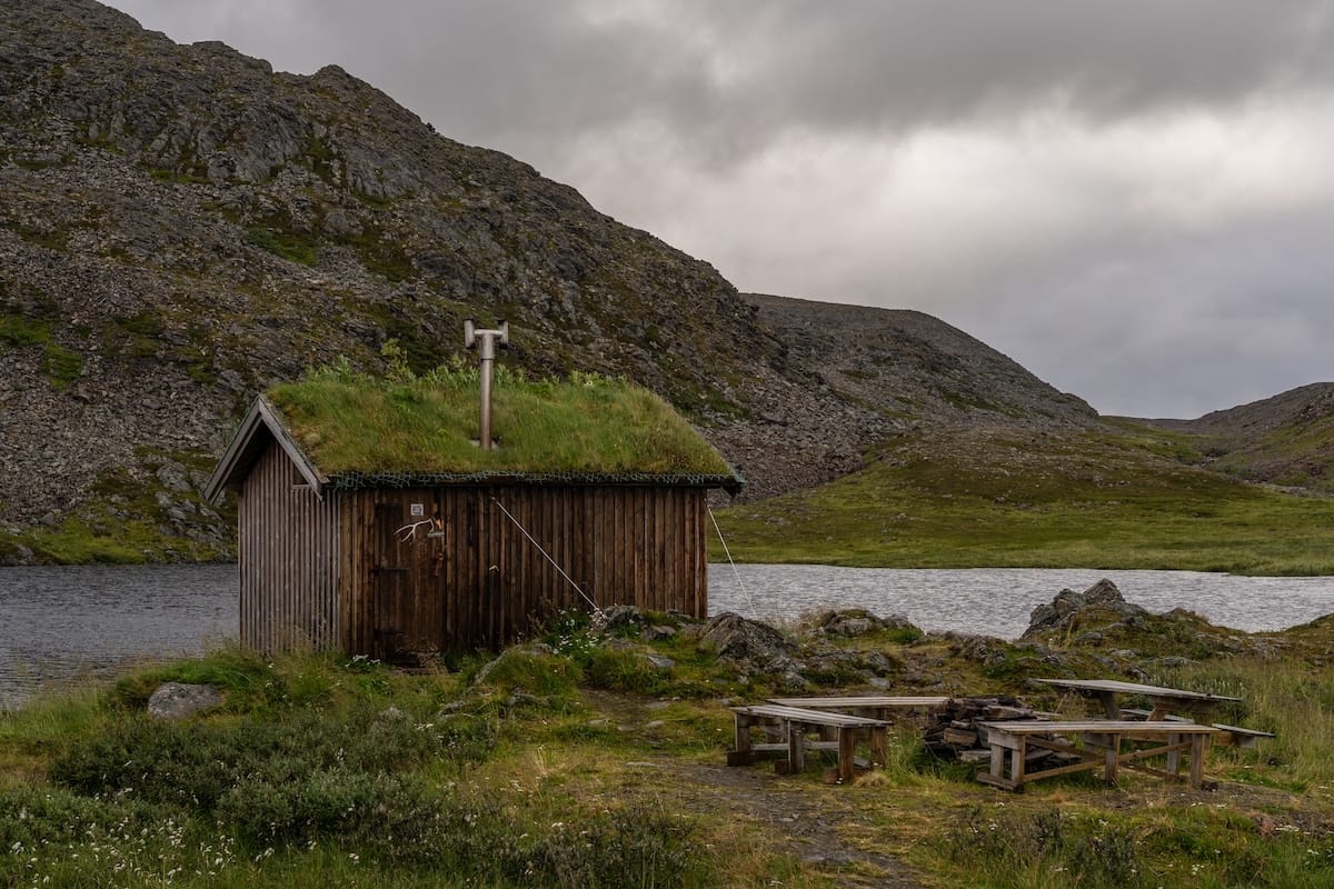 Where to Stay at the North Cape in Norway (+ Honningsvåg) a small wooden hut with a grass roof in a rocky landscape