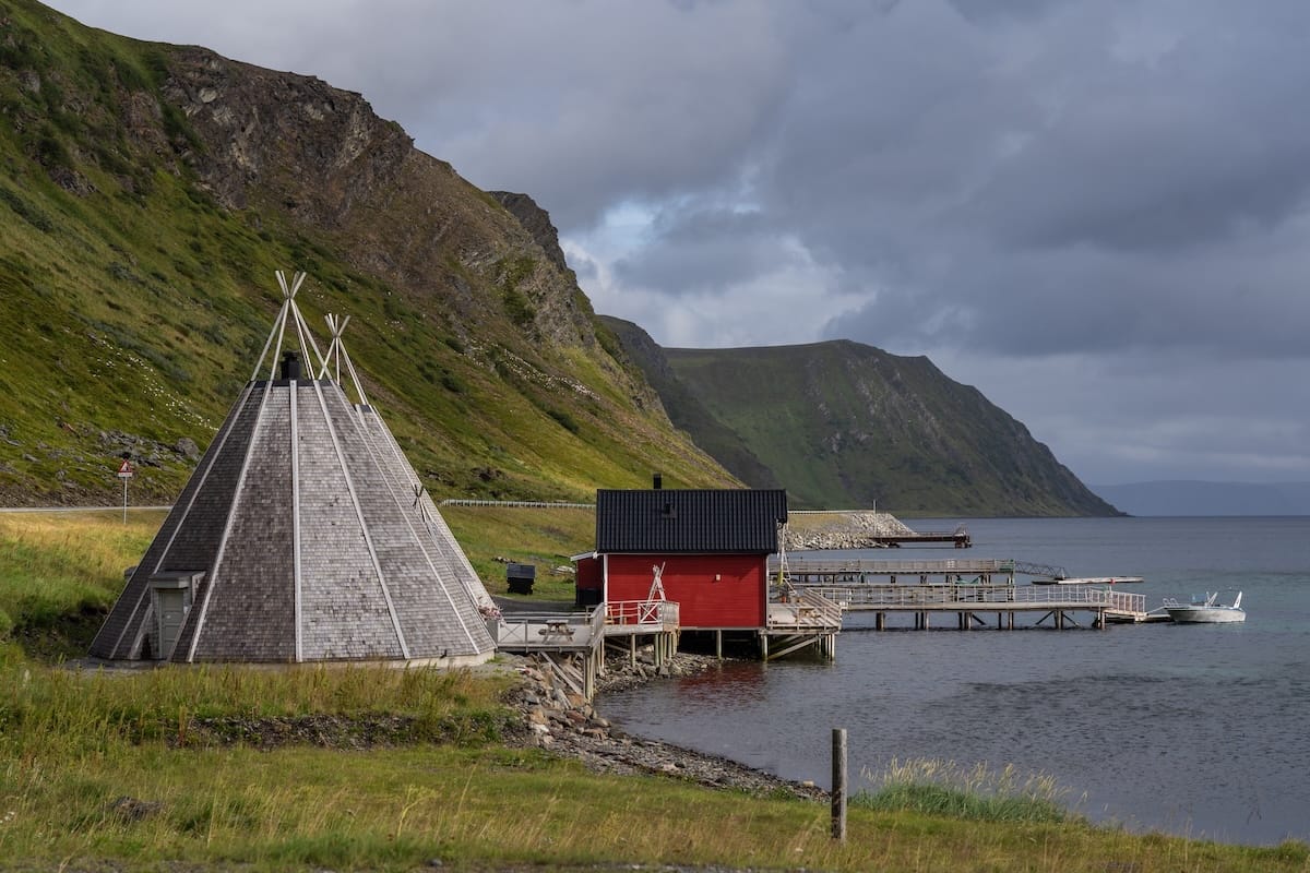 Where to Stay at the North Cape in Norway (+ Honningsvåg)
a red cabin on a fishing harbor with a small teepee building next to it