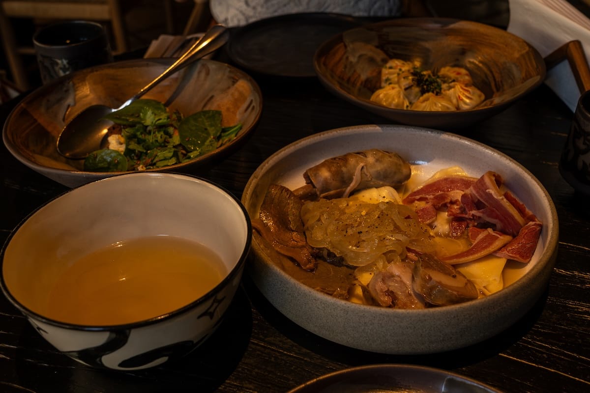 a bowl of kazakh beshbarmak with broth beside it