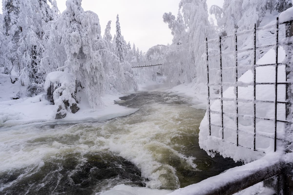 a snowy landscape with a river and a hanging bridge
